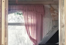 Verlassenes Zimmer mit Klavier und rosa Vorhängen.