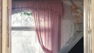 Verlassenes Zimmer mit Klavier und rosa Vorhängen.